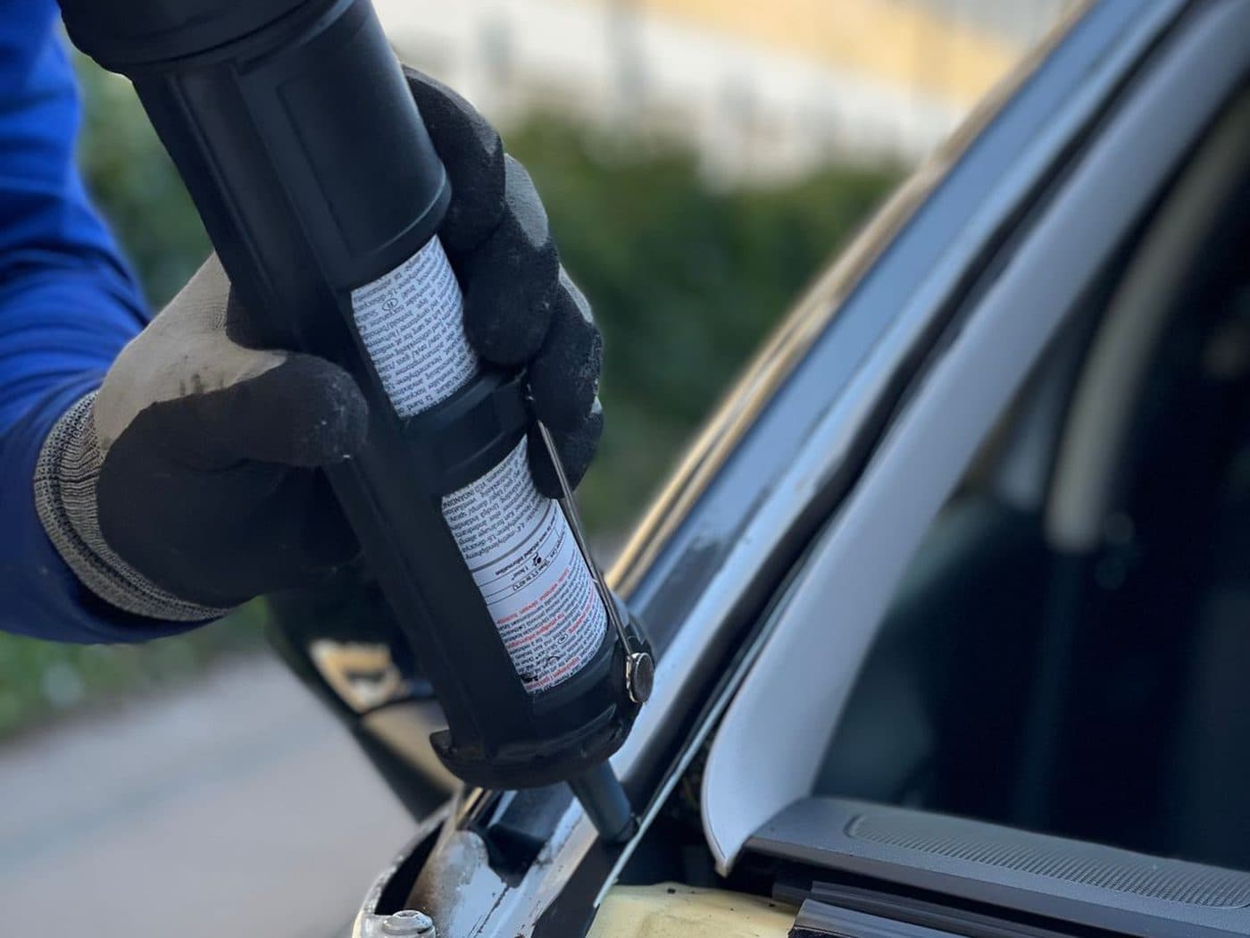 Technician applying urethane sealant to a windscreen frame during an on-site replacement